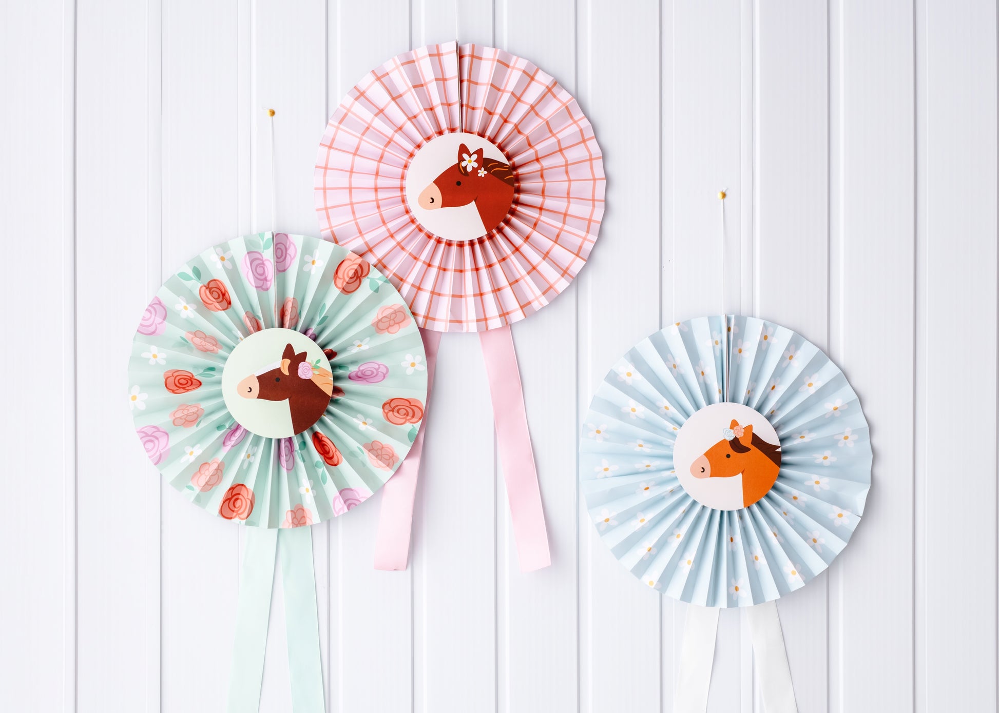 Three colorful paper fans with horse designs on a white wooden background