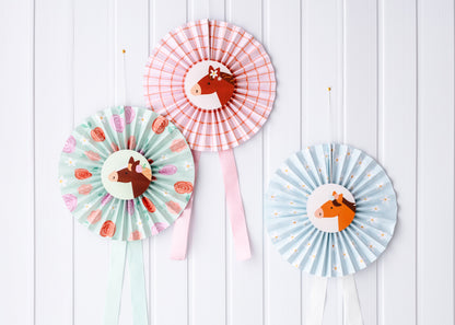 Three colorful paper fans with horse designs on a white wooden background