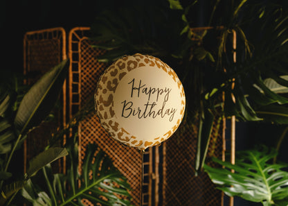 Round 'Happy Birthday' sign with leopard print border against a dark background with plants