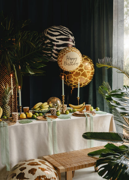 Decorative table setting with balloons, candles, and fruits in a room with dark curtains and plants.
