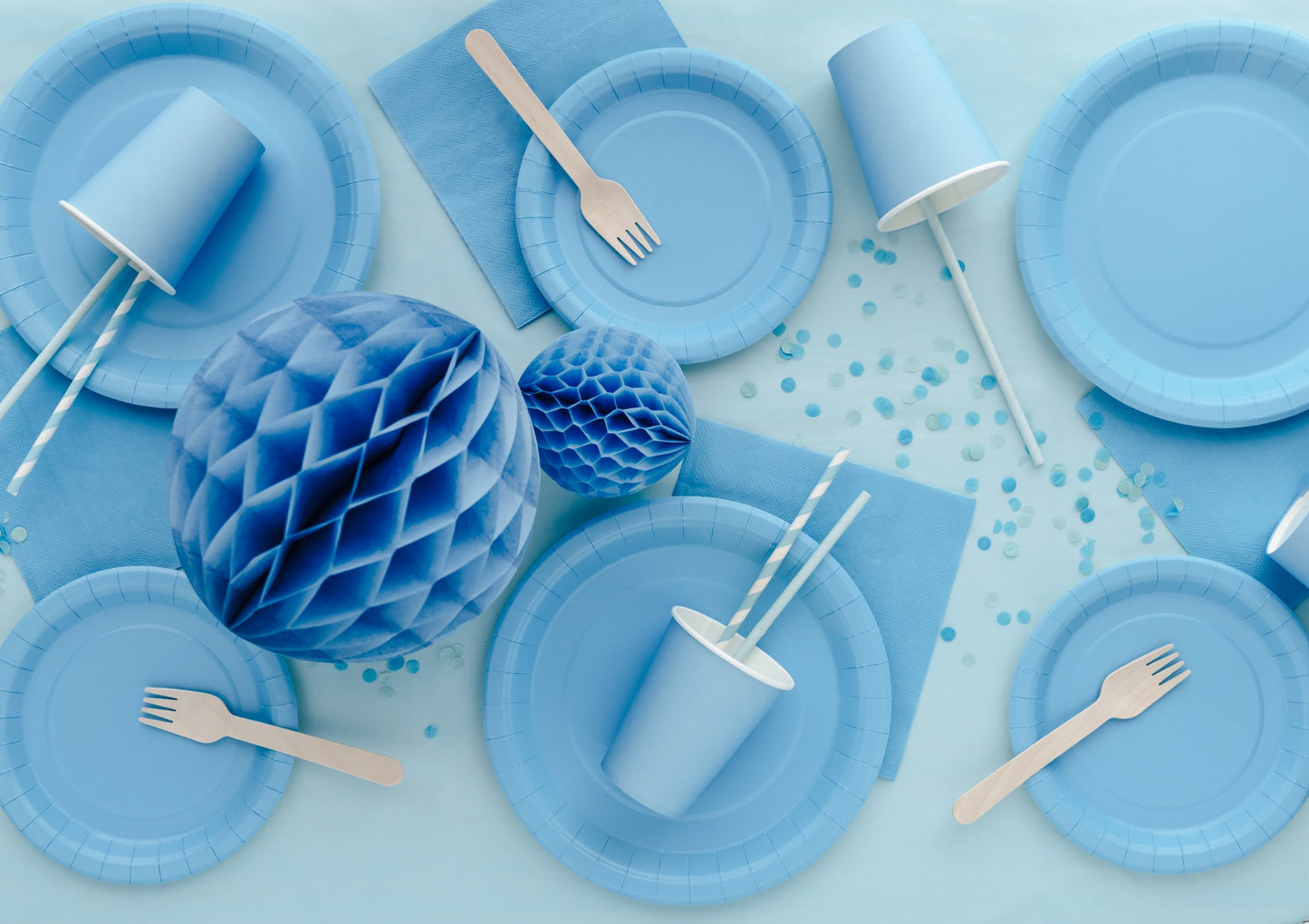 Blue party supplies including plates, cups, and decorations on a light blue background.