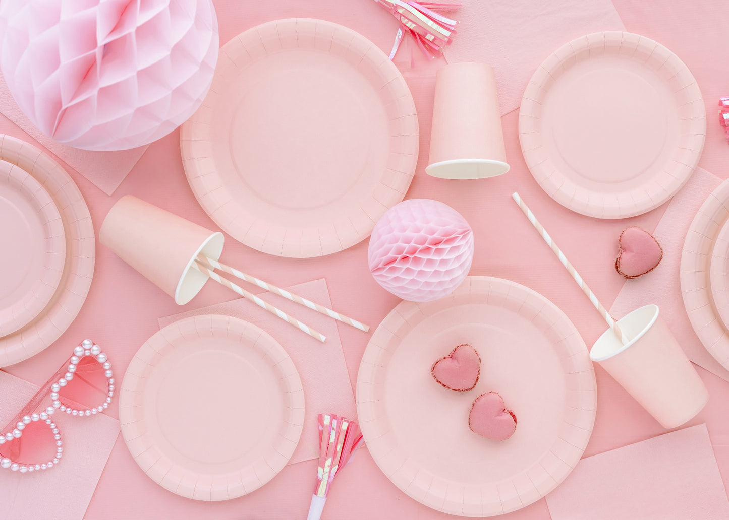 Pink party supplies including plates, balloons, and decorations on a pink background