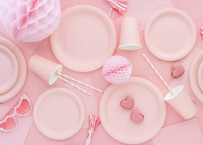 Pink party supplies including plates, balloons, and decorations on a pink background