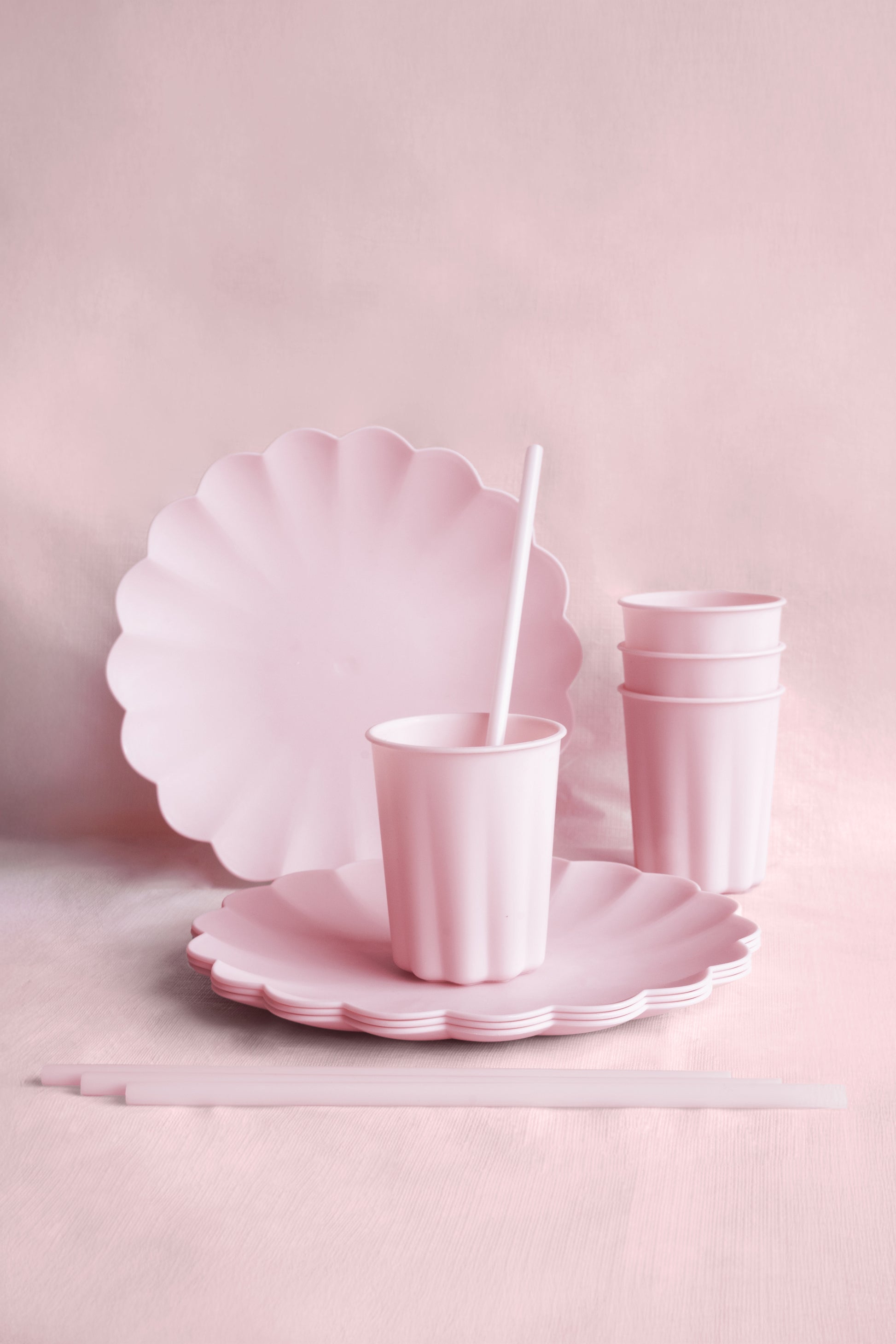 Set of pink paper plates and cups with a straw on a light pink background