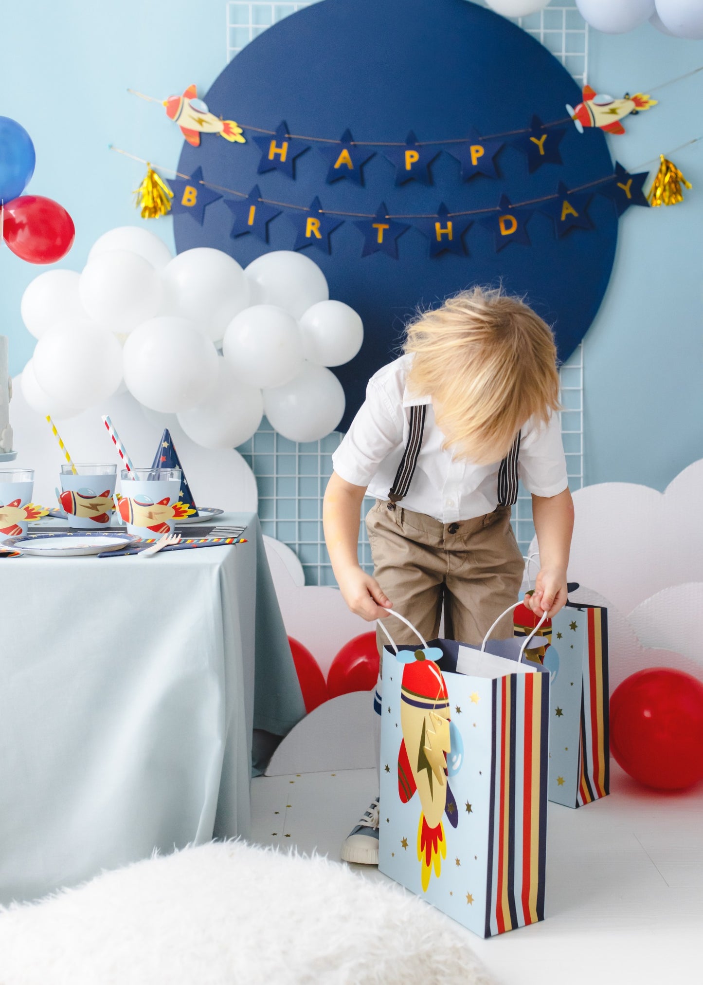 Little boy holding rocket-themed gift bags next to a decorated birthday table with space and rocket decorations