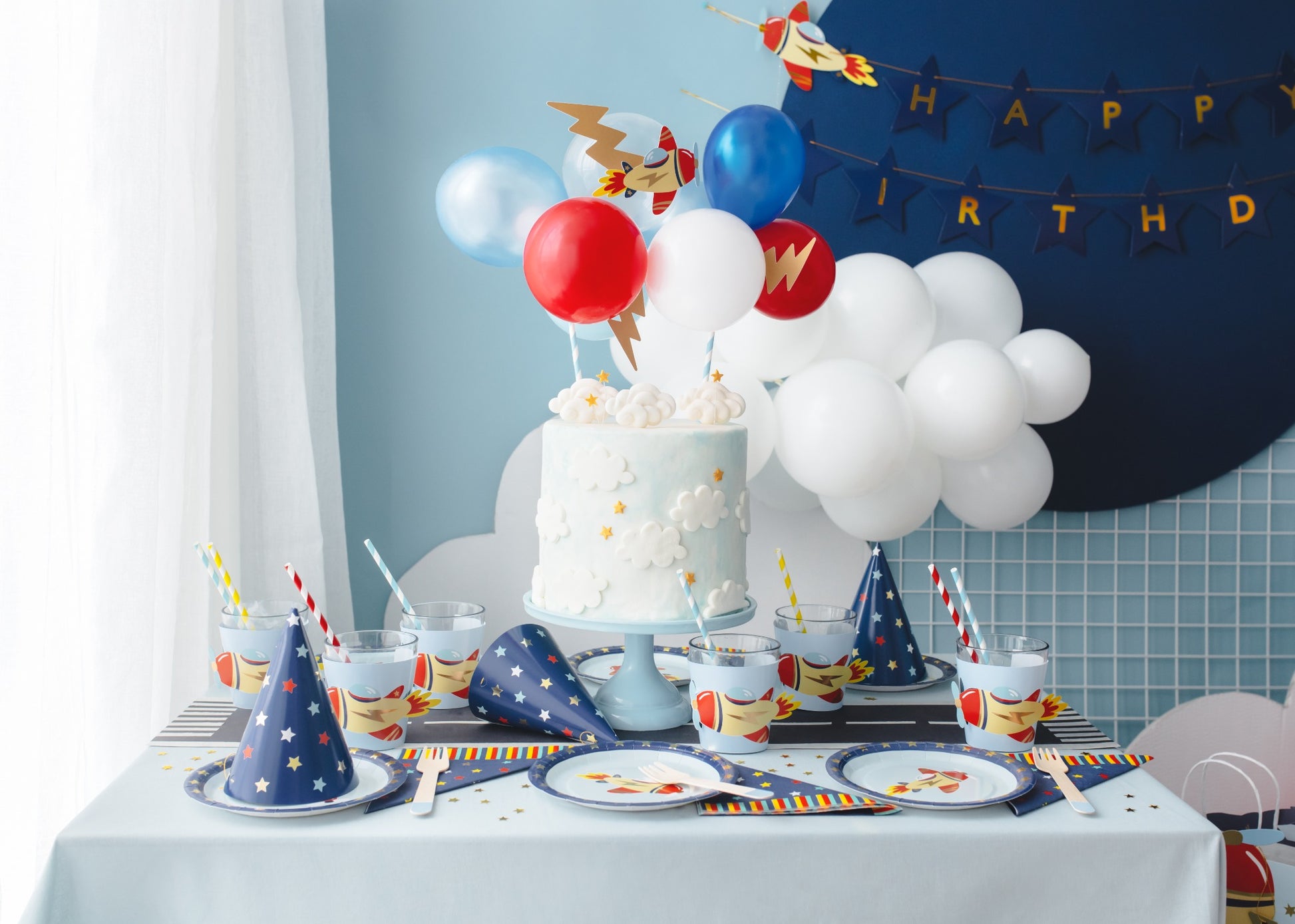 Birthday party table with a rocket runway centerpiece, rocket cups, plates, napkins, and party hats in space theme