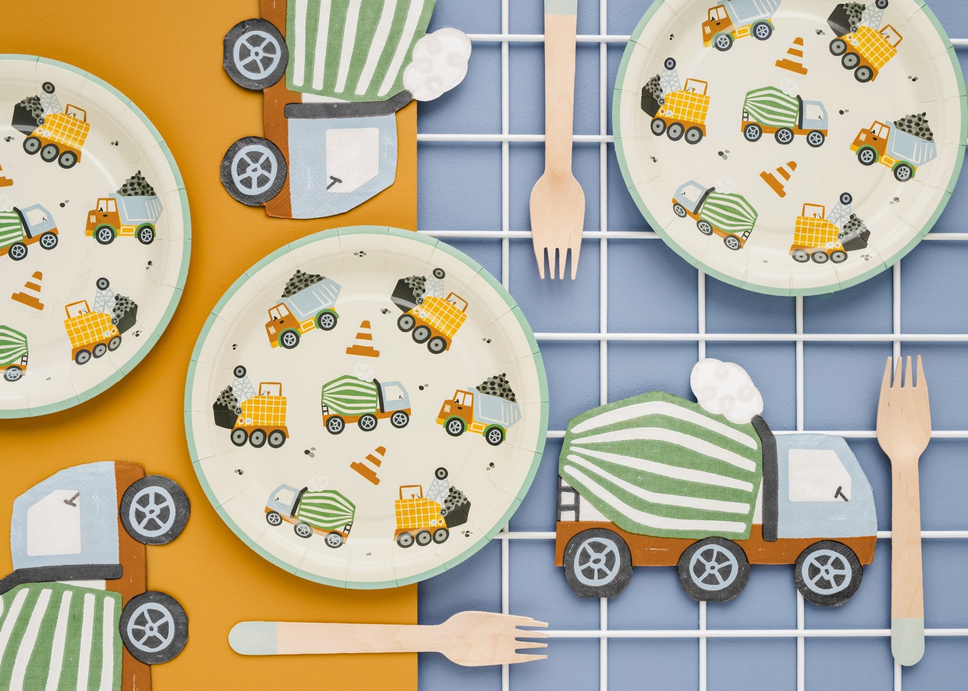 Paper plates decorated with cement trucks, dump trucks, and traffic cones, styled with wooden forks for a kids' construction birthday party