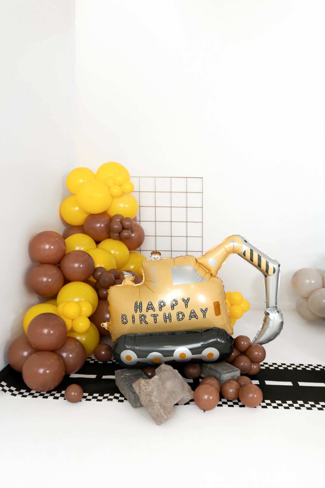 Foil balloon shaped like an excavator with 'Happy Birthday' text, surrounded by yellow and brown balloon decorations