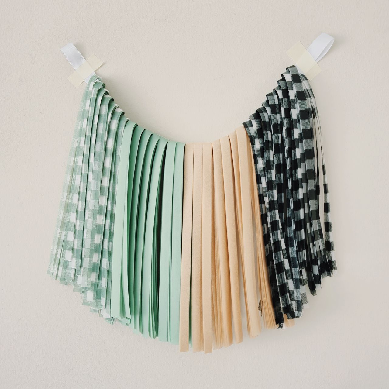 Three fabric swatches in green checkered, beige, and black and white pattern hanging on a line against a beige background.