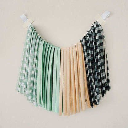 Three fabric swatches in green checkered, beige, and black and white pattern hanging on a line against a beige background.