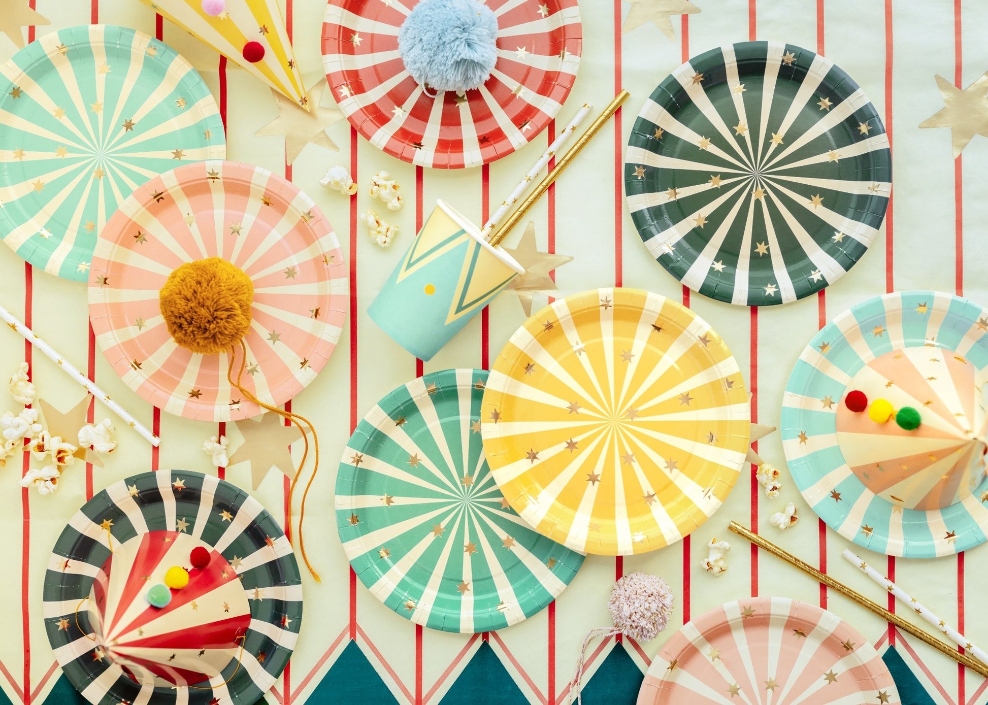 Colorful set of round paper plates with circus stripe patterns in yellow, pink, turquoise, red and dark green, decorated with golden stars