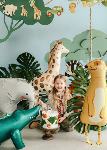 Child with a cake surrounded by inflatable animal decorations in a jungle-themed room.