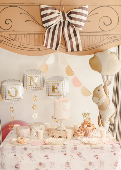 Decorated birthday table with cake, balloons, and a large bow on the wall.