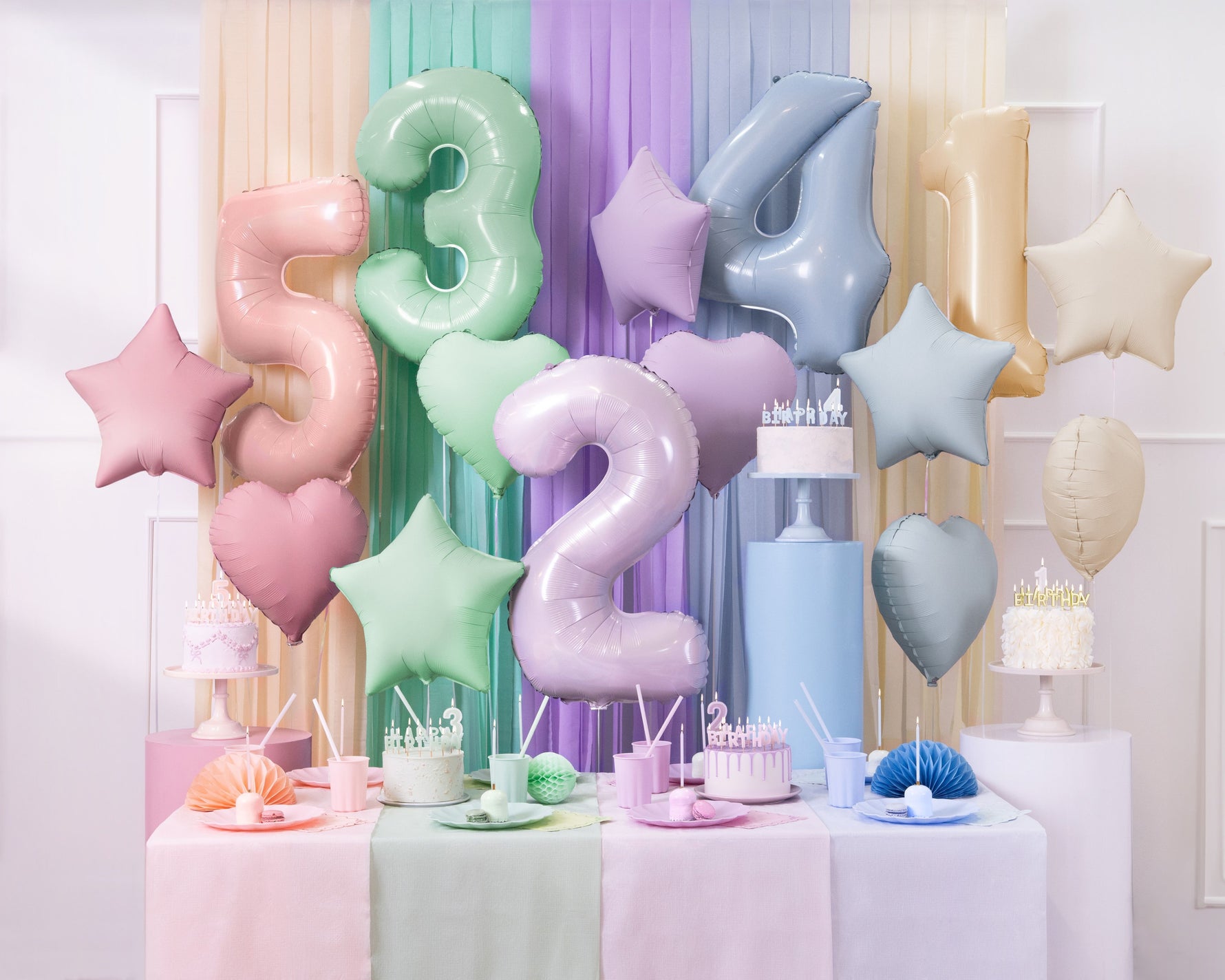 Pastel-colored balloons shaped like numbers and stars amd birthday cakes with candles.