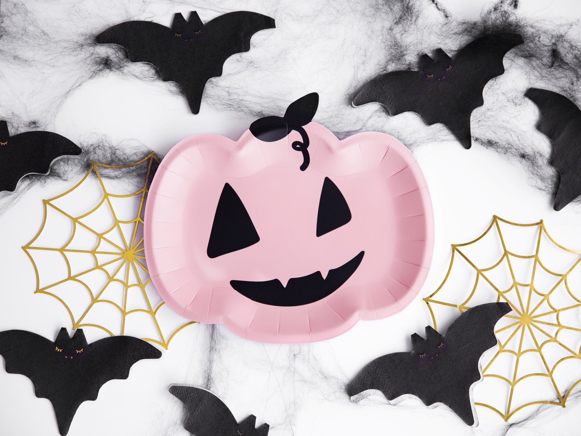 Pink paper plate shaped like a jack-o'-lantern with black bats and spider webs on a white background