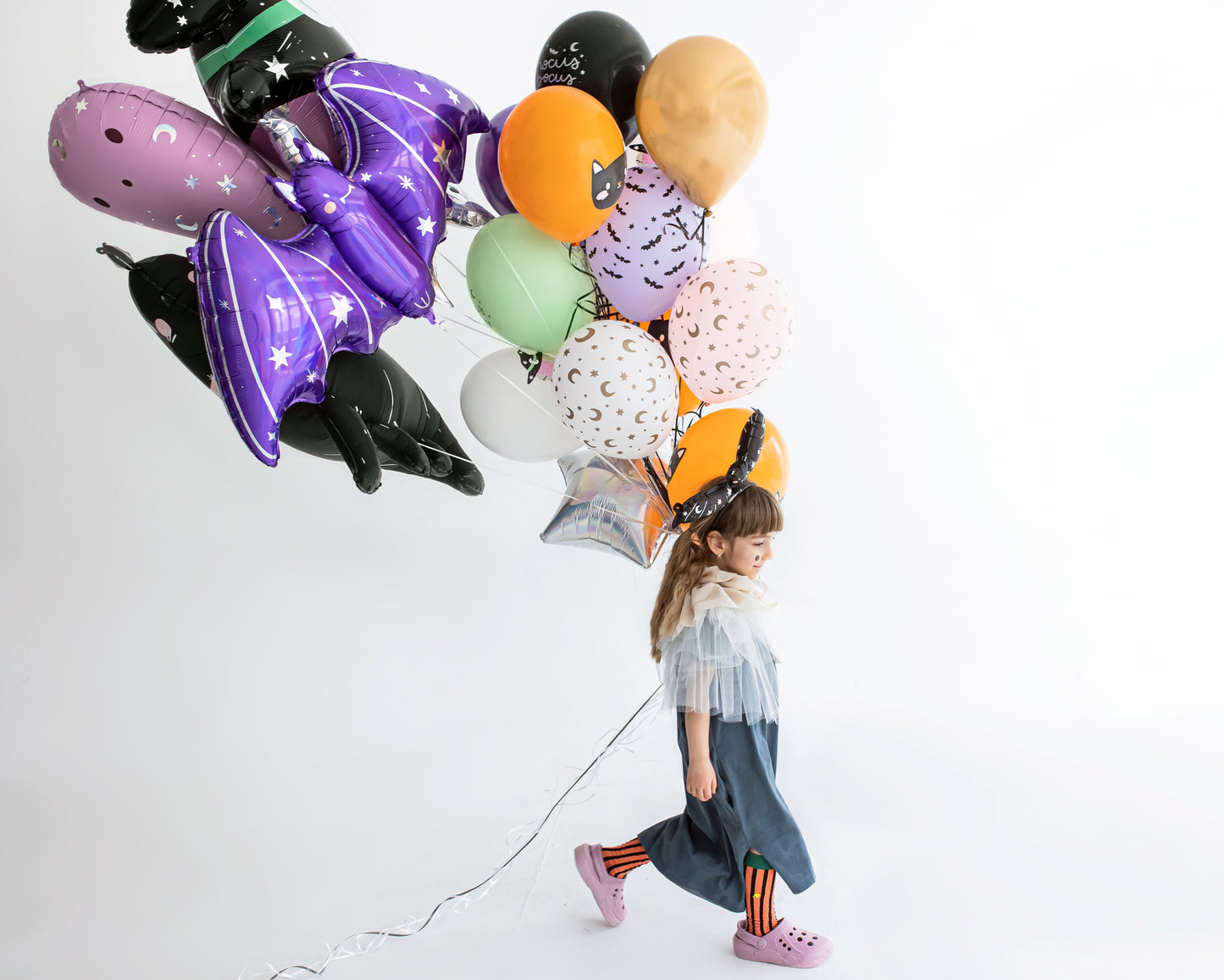 Child holding Halloween-themed balloons against a white background