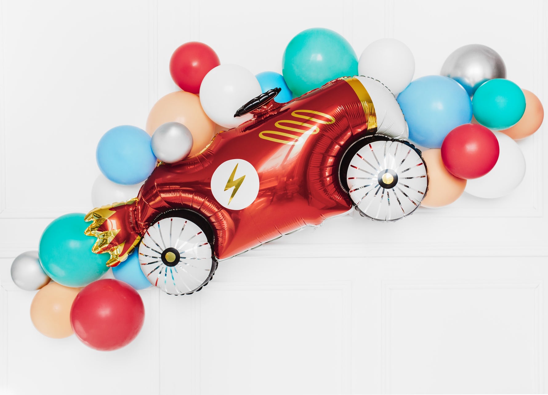 Red car-shaped balloon surrounded by colorful latex balloons on a white background