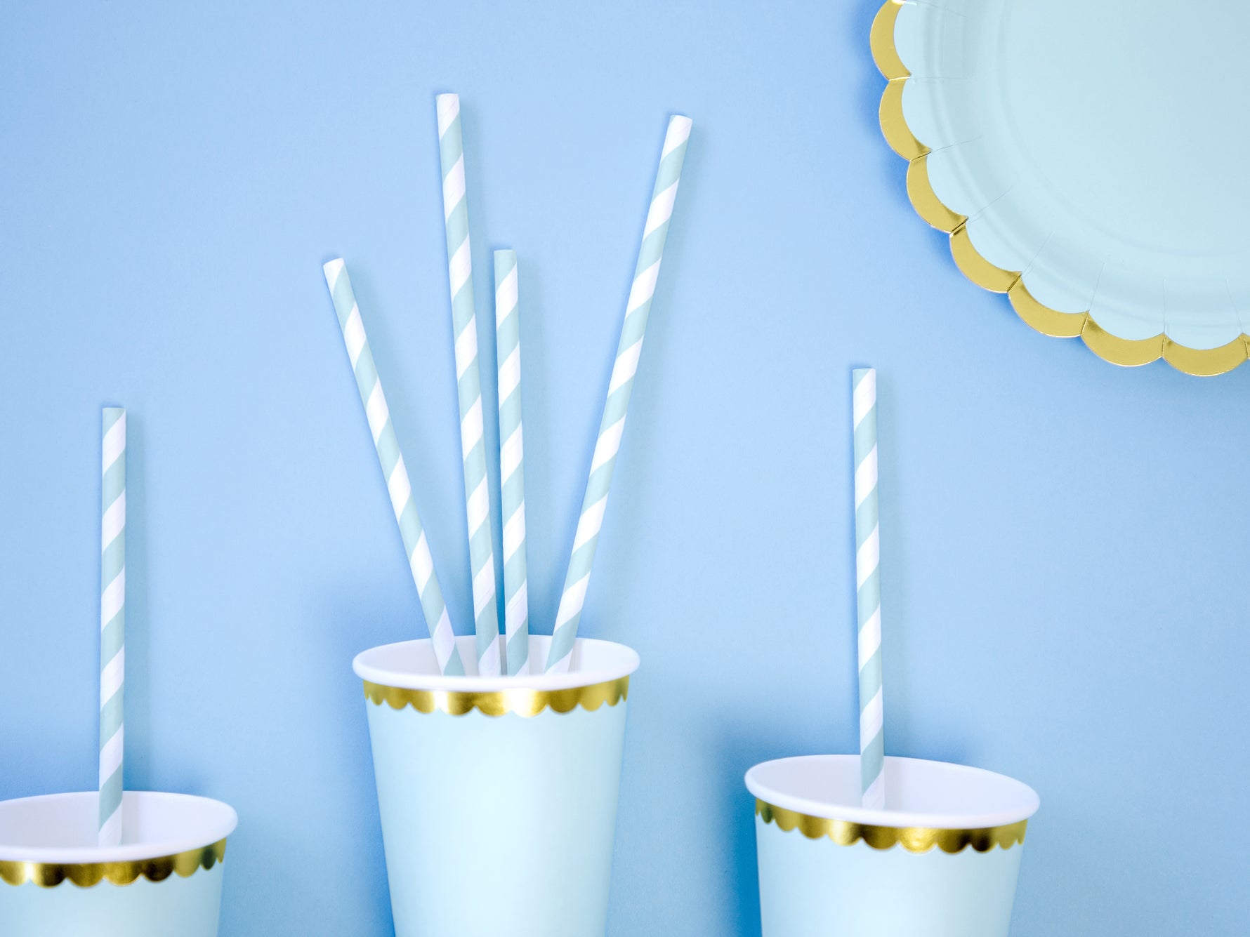 White paper cups with gold trim and striped straws on a light blue background