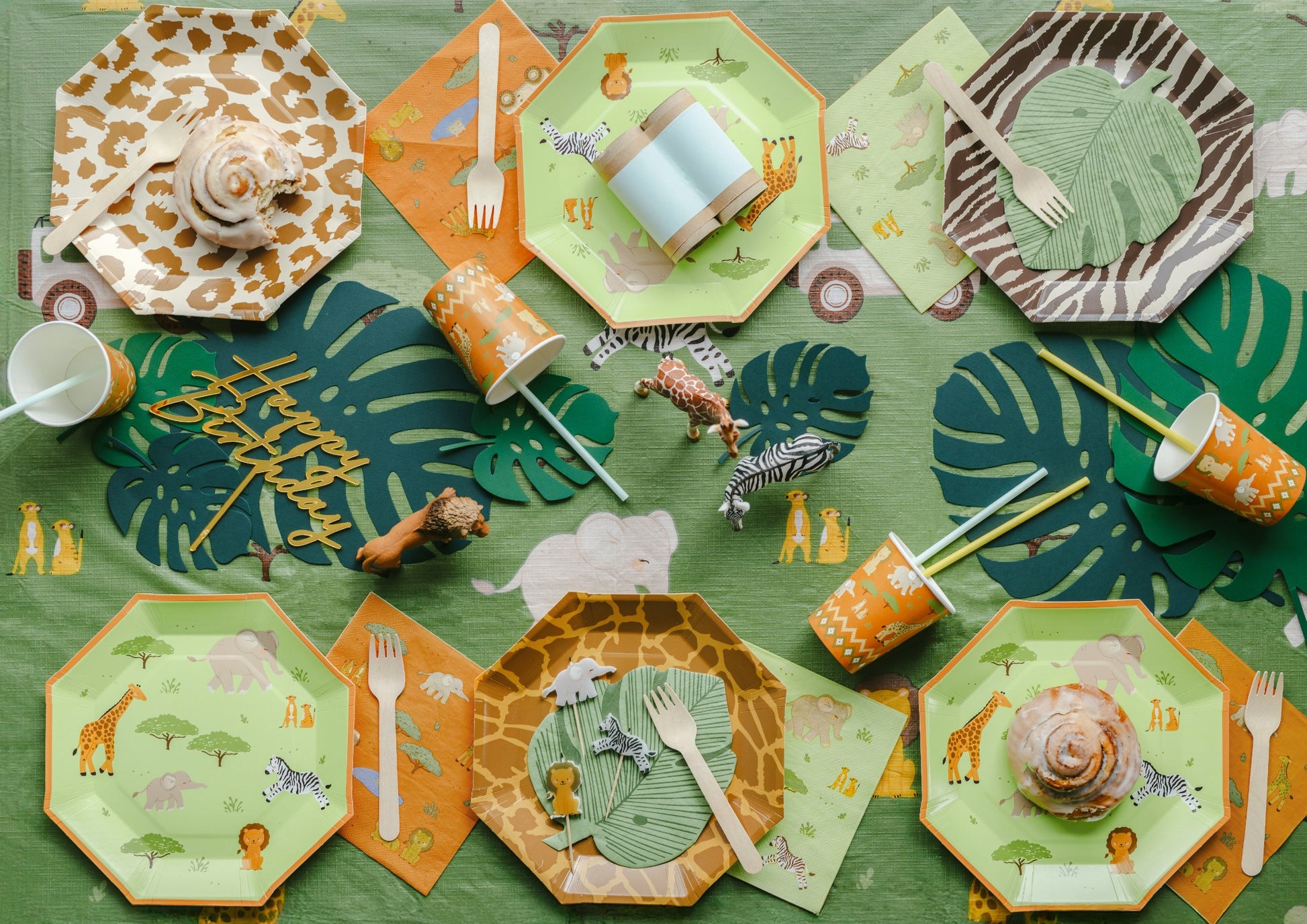 Children's party table setting with jungle-themed plates, cups, and utensils on a green tablecloth.