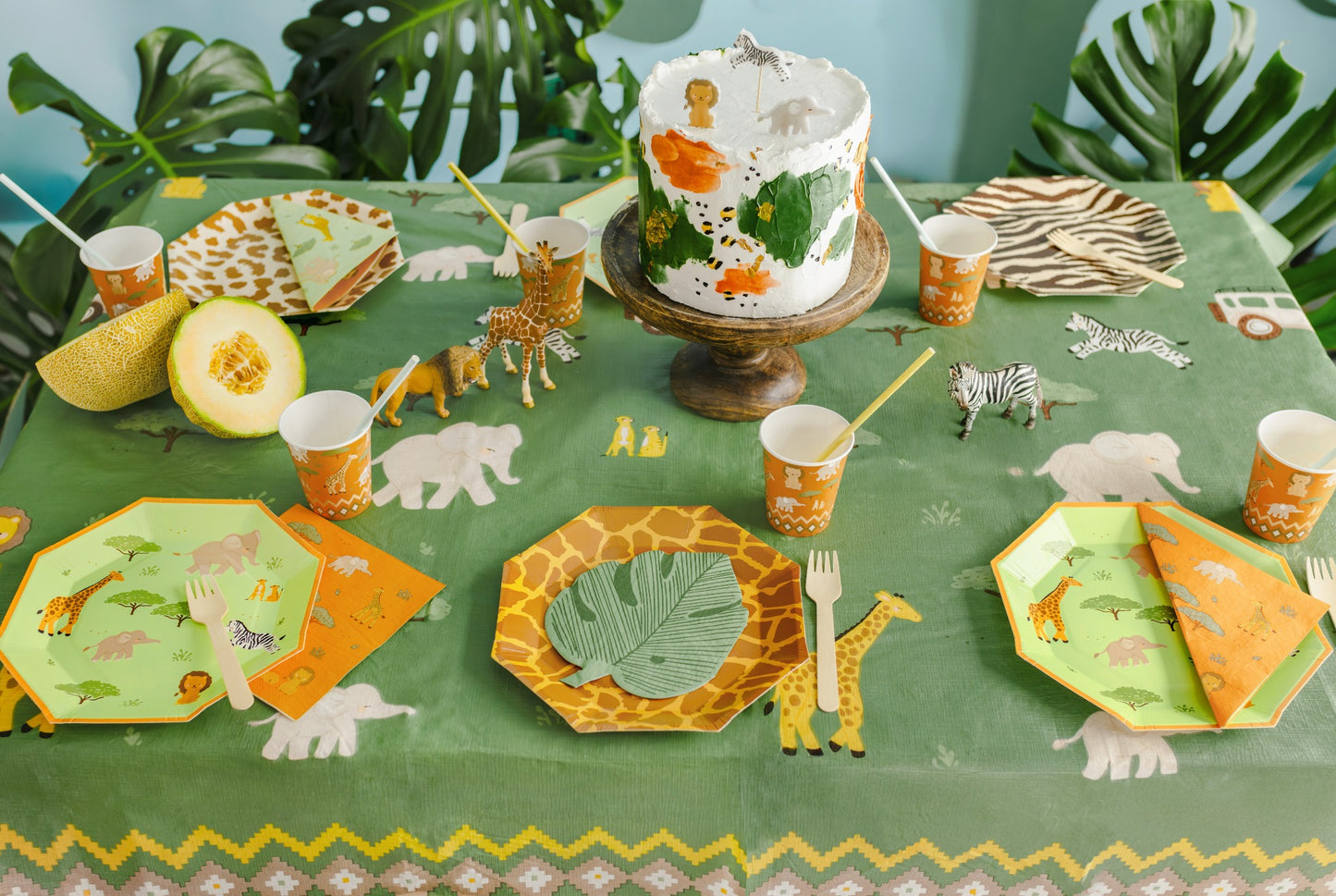 Jungle-themed party setup with cake, plates, cups, and decorations on a green tablecloth.