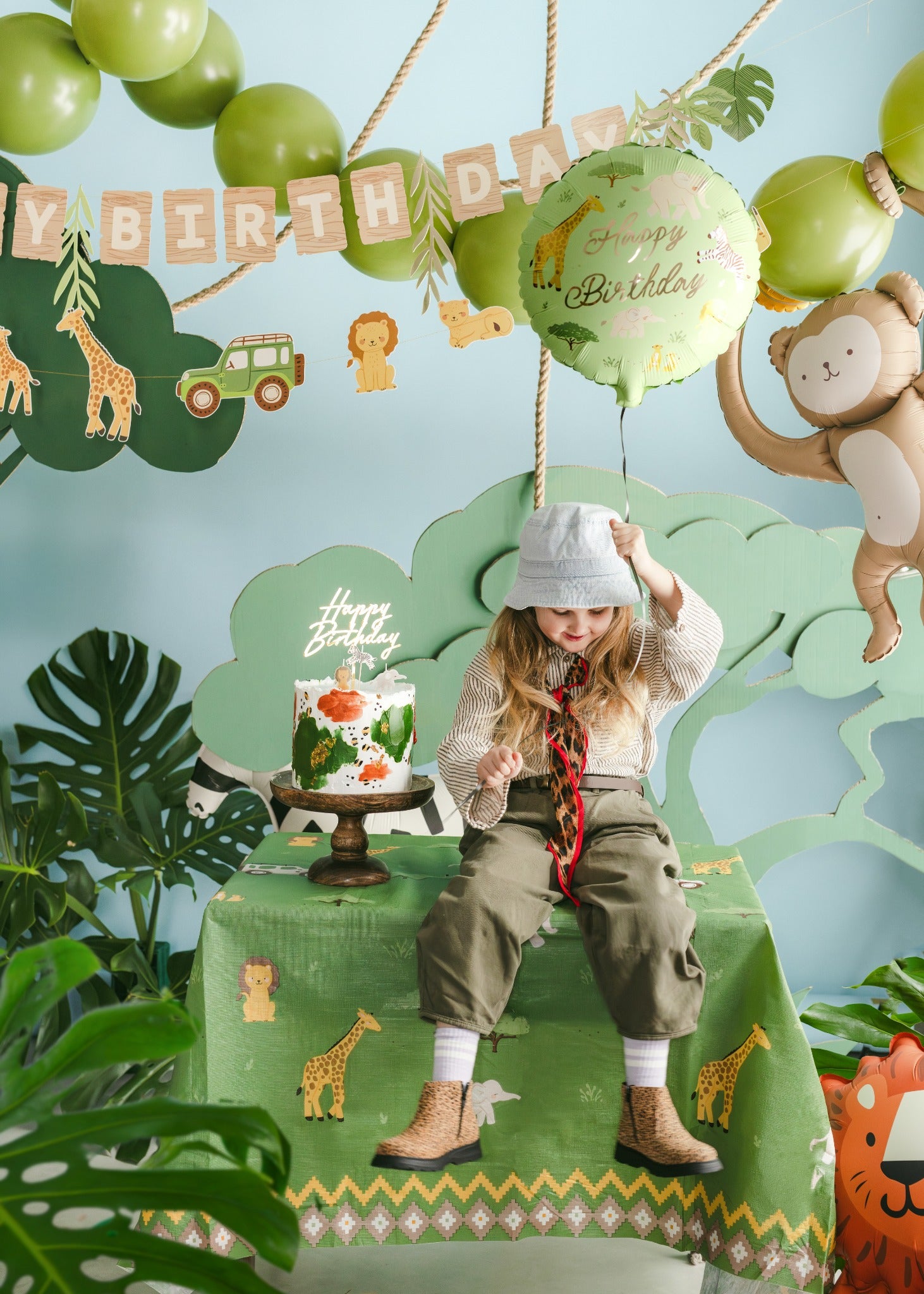 Child at a birthday party with green decorations, balloons, and a cake.