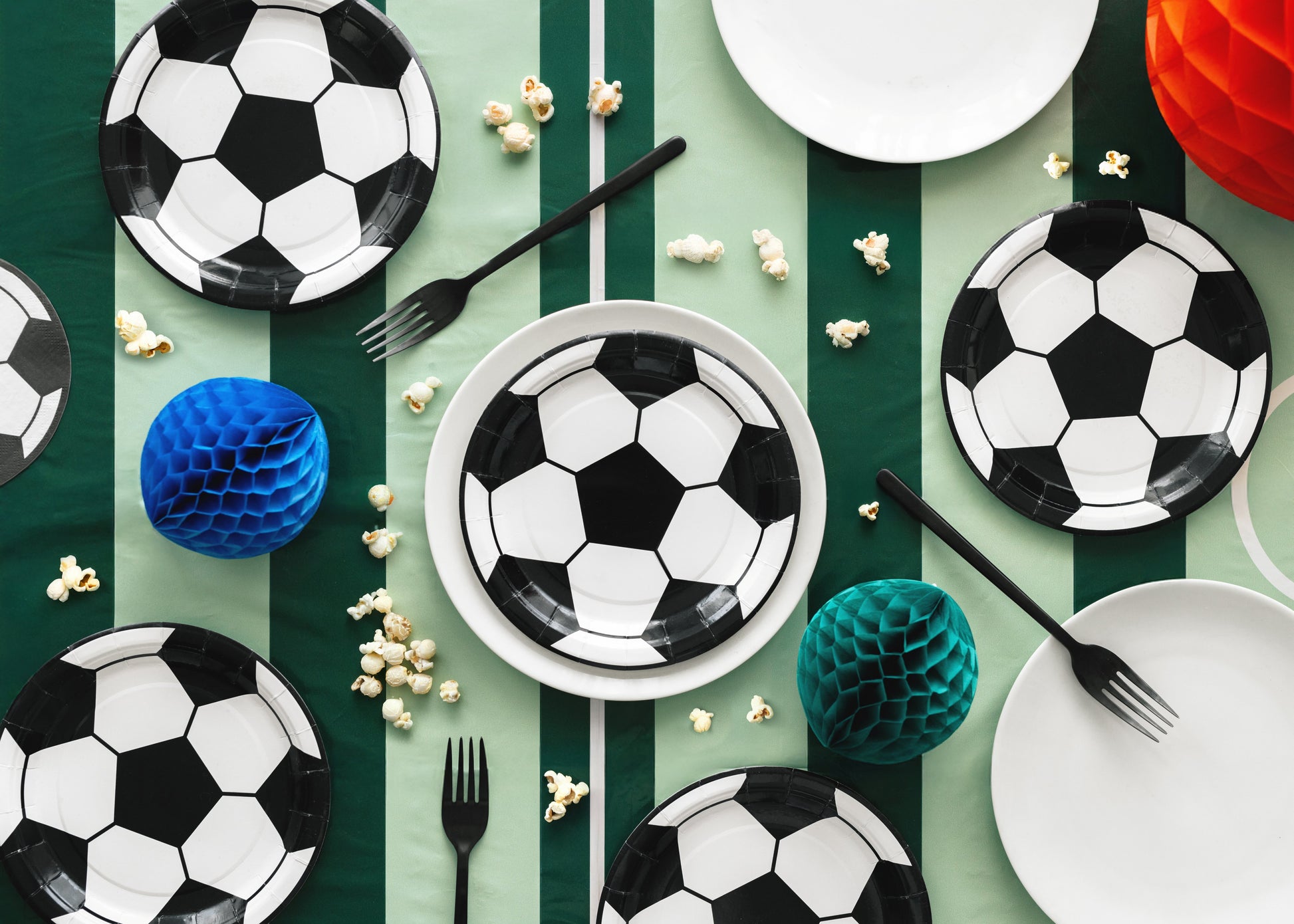 Soccer-themed table setting with plates, forks, and decorative items on a green and white striped tablecloth.