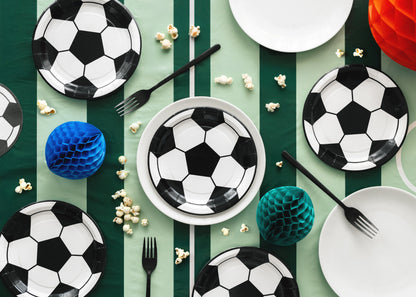 Soccer-themed table setting with plates, forks, and decorative items on a green and white striped tablecloth.