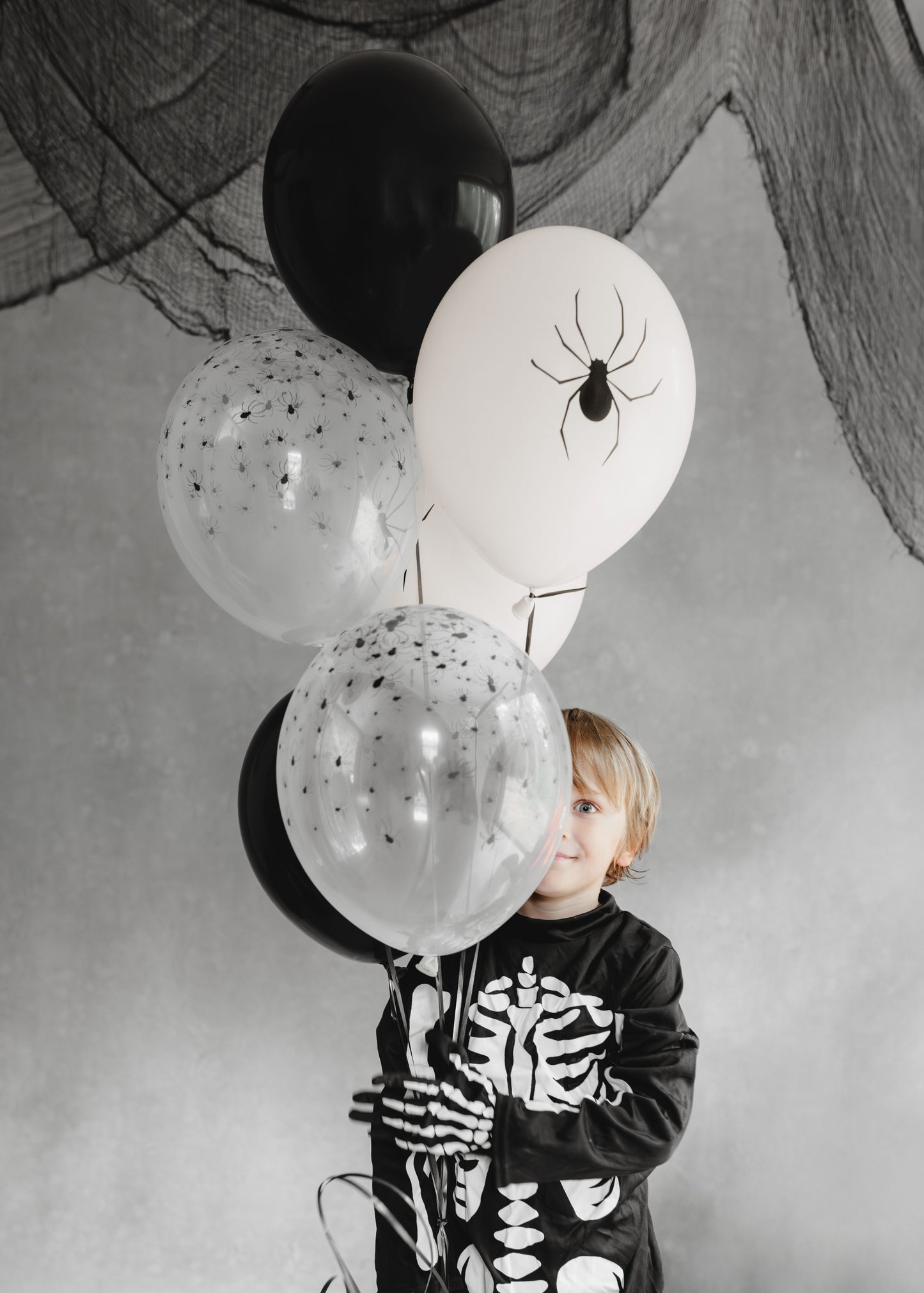 Child in a skeleton outfit holding Halloween-themed balloons with black and white colors.