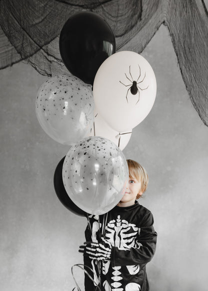 Child in a skeleton outfit holding Halloween-themed balloons with black and white colors.