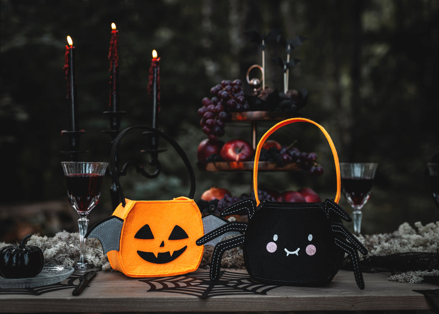 Halloween-themed candy buckets on a table with candles and fruit.