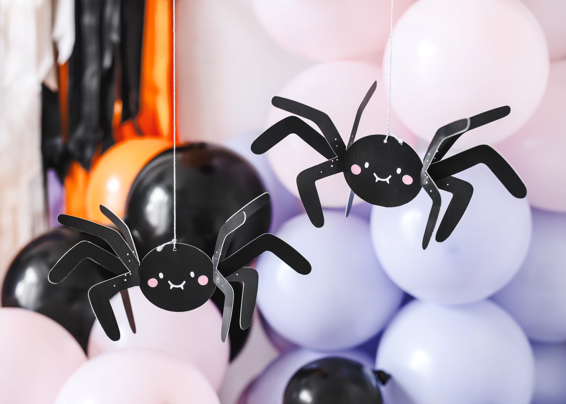 Halloween-themed decorations with spider-shaped balloons and black balloons against a pink and orange background.