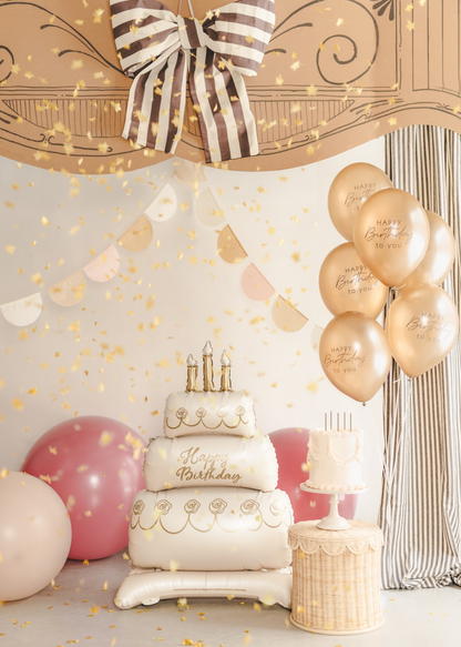 Birthday cake with candles and balloons against a decorative wall with a bow.
