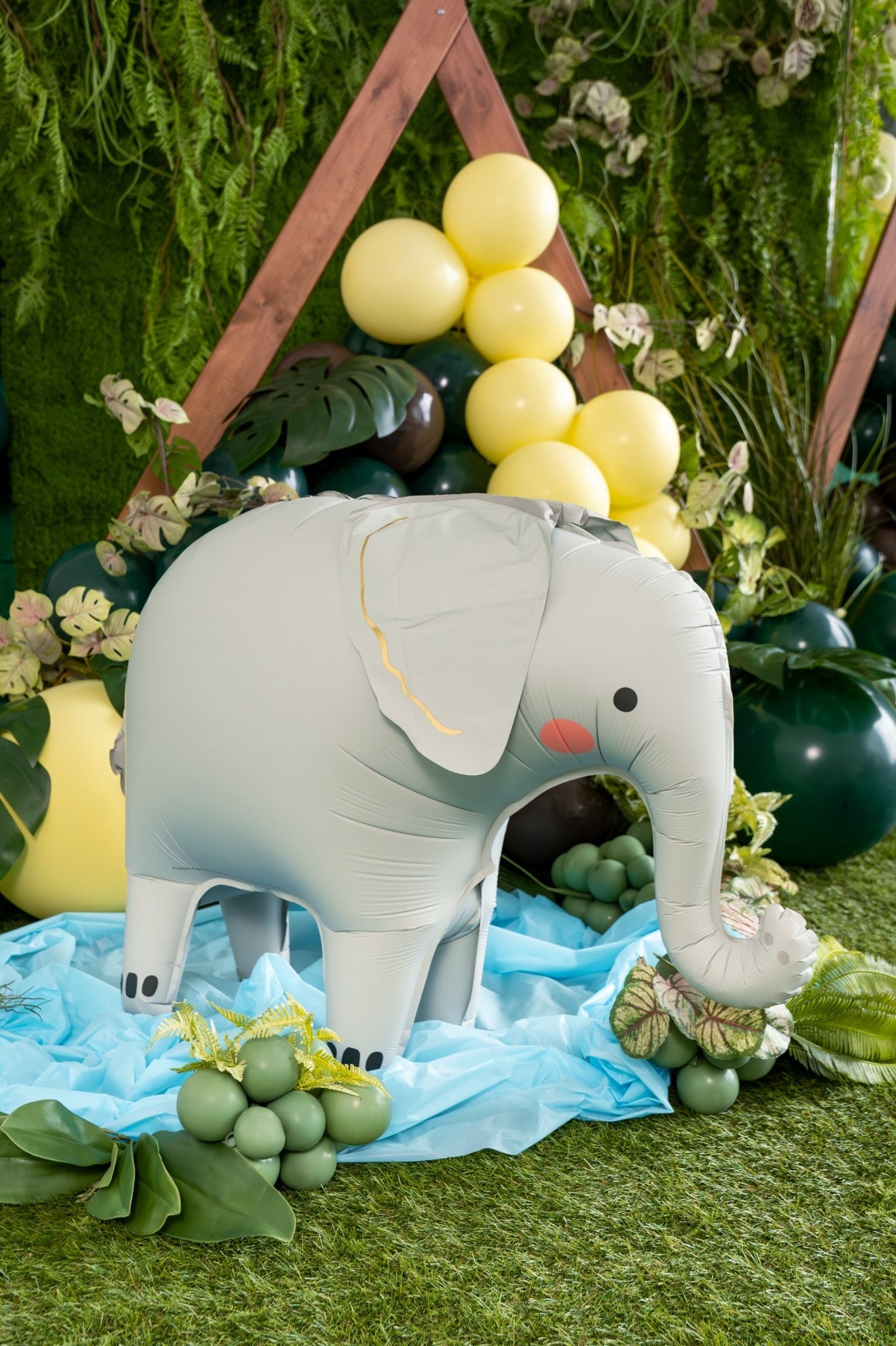 Inflatable elephant decoration on a grassy background with balloons and flowers.