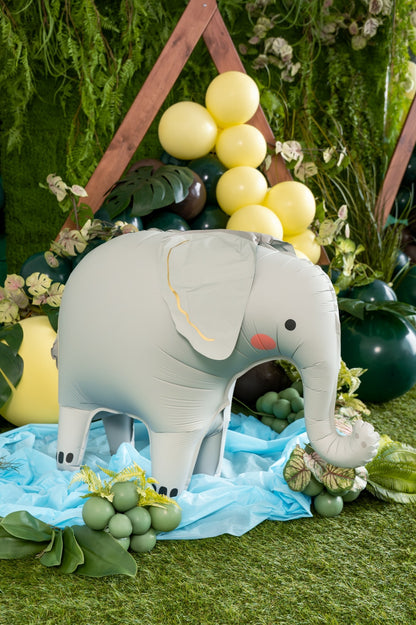 Inflatable elephant decoration on a grassy background with balloons and flowers.
