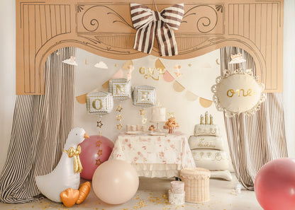 Decorative setup with balloons, cake, and tablecloth in a room with curtains and a decorative arch.