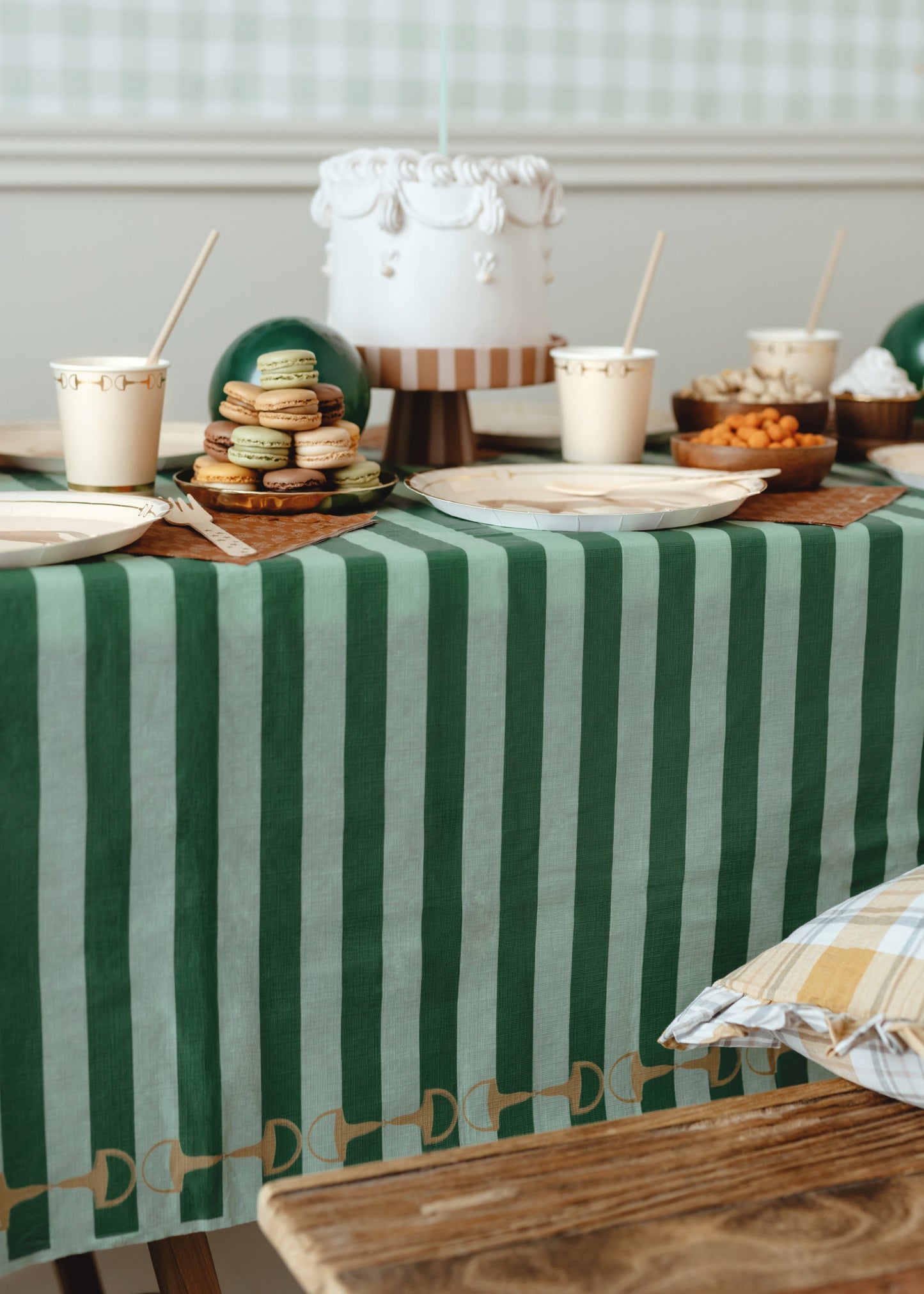 Table setting with a green and white striped tablecloth, plates, and a cake.