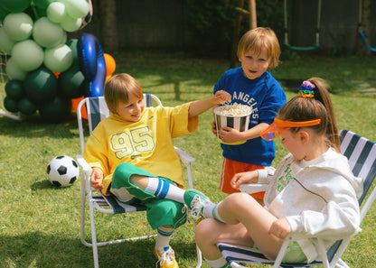 Children sitting on lawn chairs with popcorn and balloons in a backyard setting