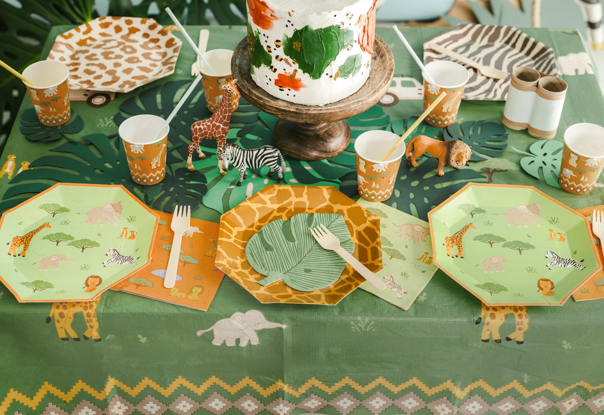 Children's table setting with jungle-themed plates, cups, and decorations on a green tablecloth.