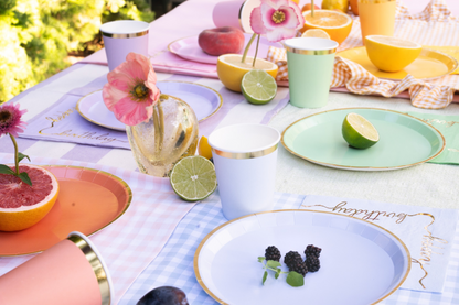 Pastel birthday tableware with gold-rimmed cups and plates, fresh citrus fruits, and vibrant flowers – elegant kids party table setting