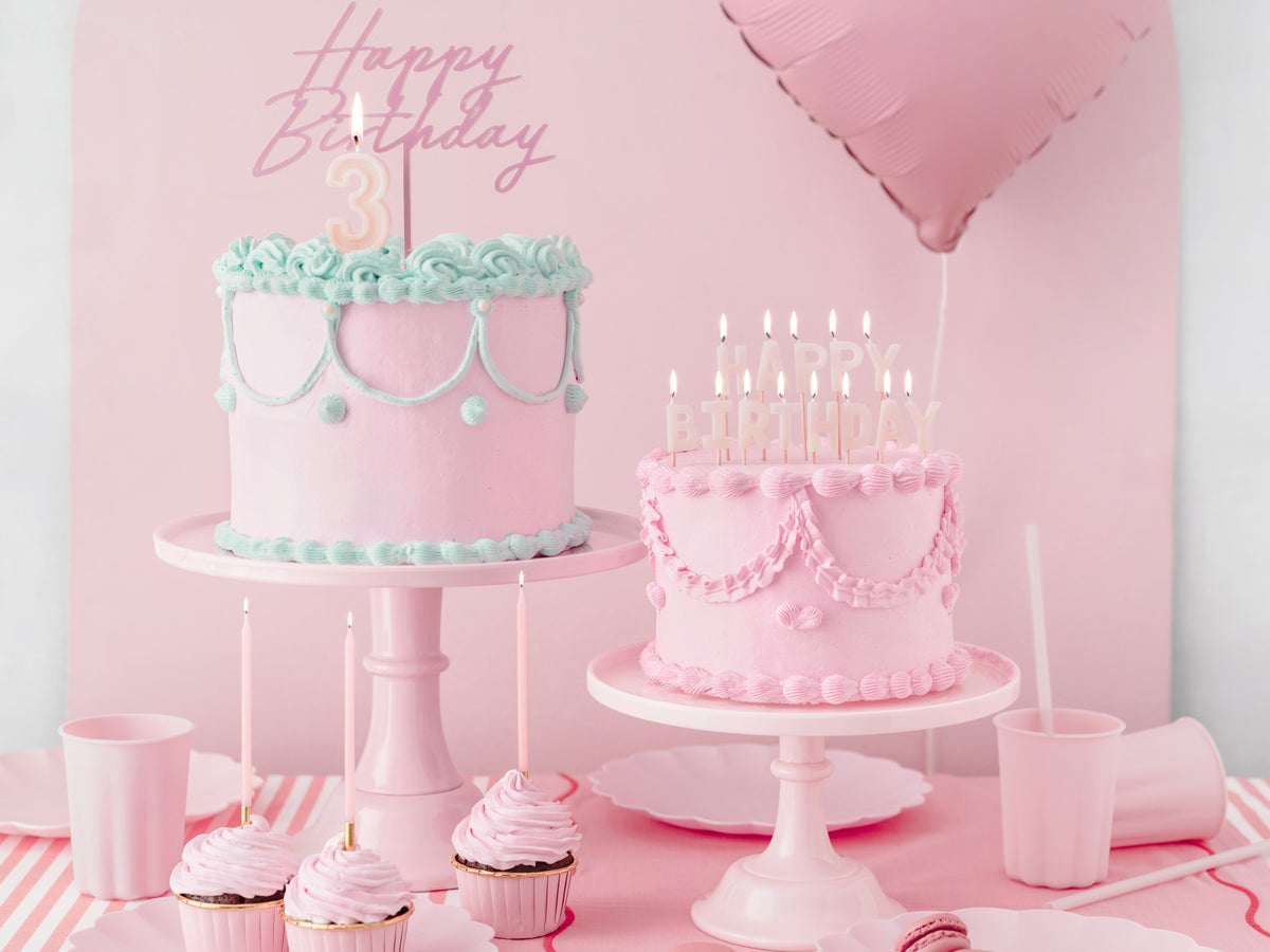 Two birthday cakes on stands with pink decorations.