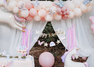 Balloon arch with small butterflies in pink and blue colors with 'Happy Birthday' banner in the middle matching unicorn-themed party.
