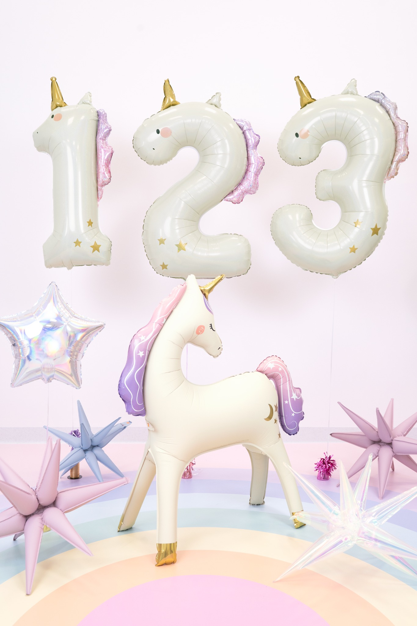Unicorn-shaped number balloons with a small unicorn figurine on a colorful background