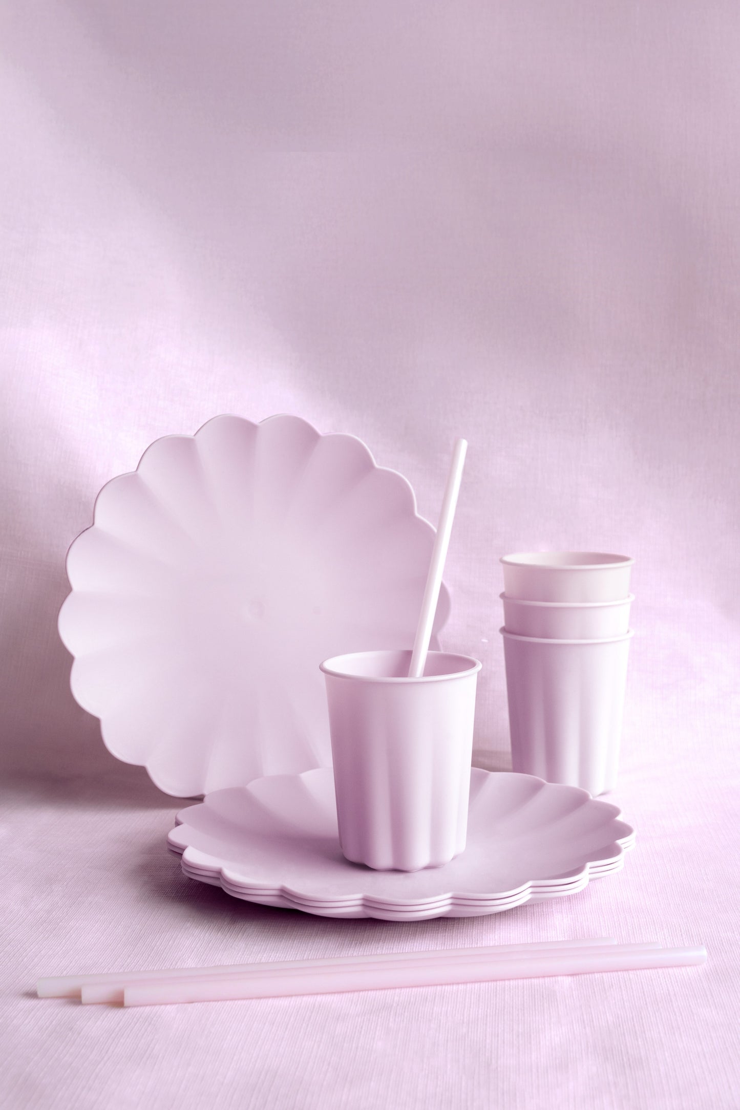 Set of white scalloped plates and cups on a light pink background