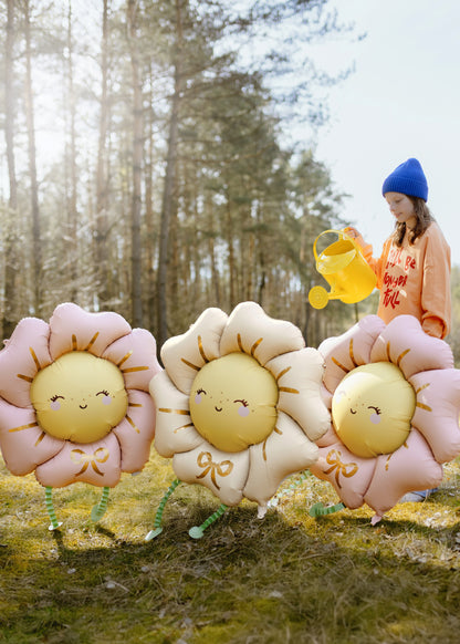 Three smiling flower-shaped balloon with legs in a forest setting, with a child holding a yellow watering can.