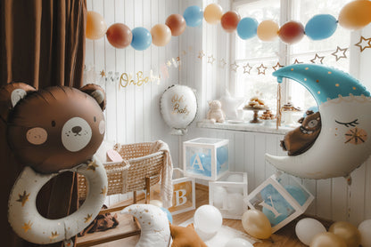 Neutral baby shower decor with teddy bear and moon foil balloons, Oh Baby banner, balloon garland, white wooden cradle, and ABC blocks – cozy setup for welcoming a newborn baby boy or girl.