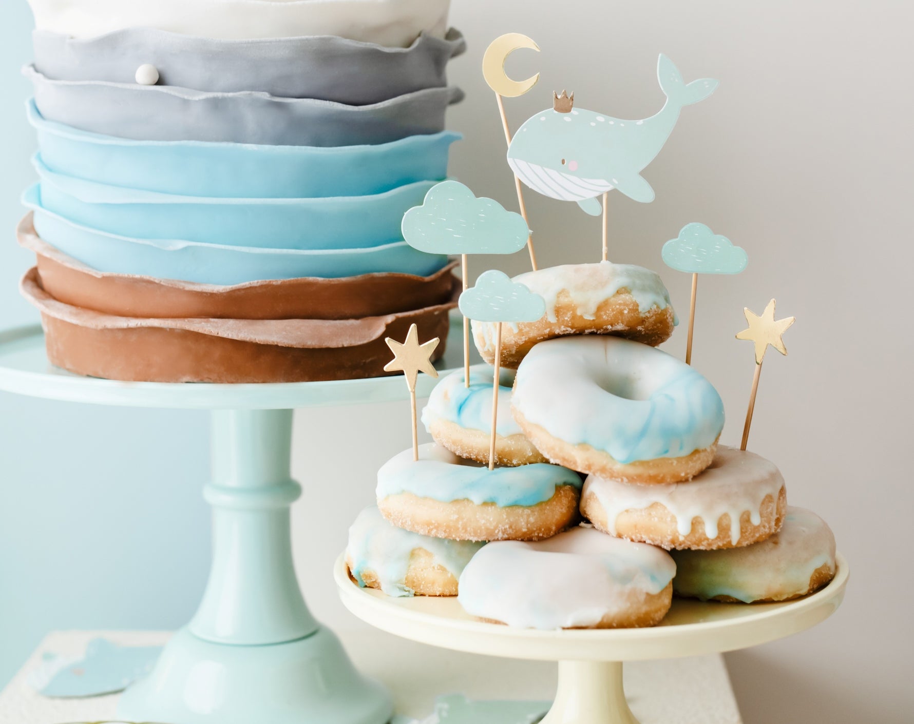 Birthday cake with blue and brown layers next to a tower of donuts with decorative narwhal toppers.
