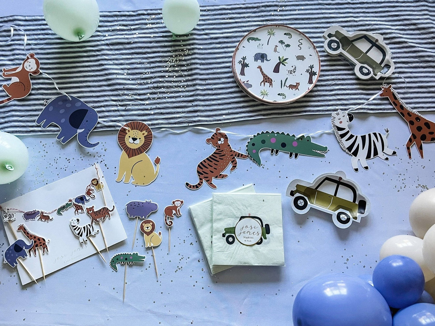 Children's party decorations with animal-themed paper plates, napkins, and balloons on a striped tablecloth.