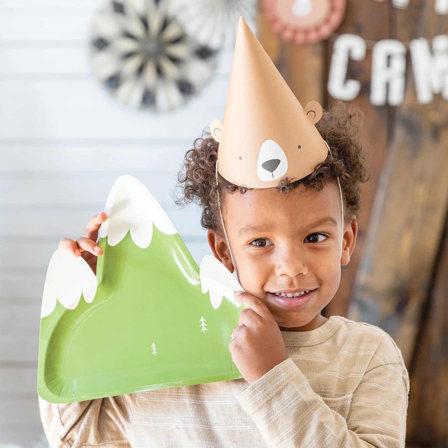 Child wearing a bear hat holding a green mountain-shaped plate with white snow.