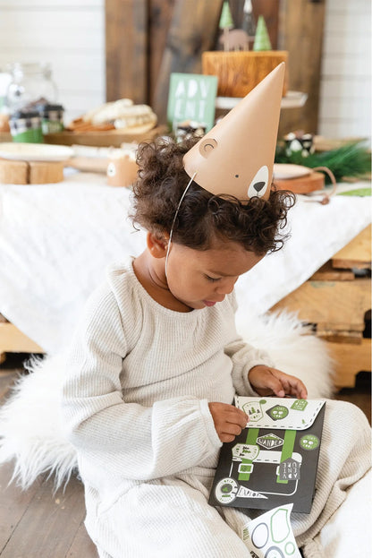 Child wearing a bear party hat sitting on a white chair indoors with backpack treat bag