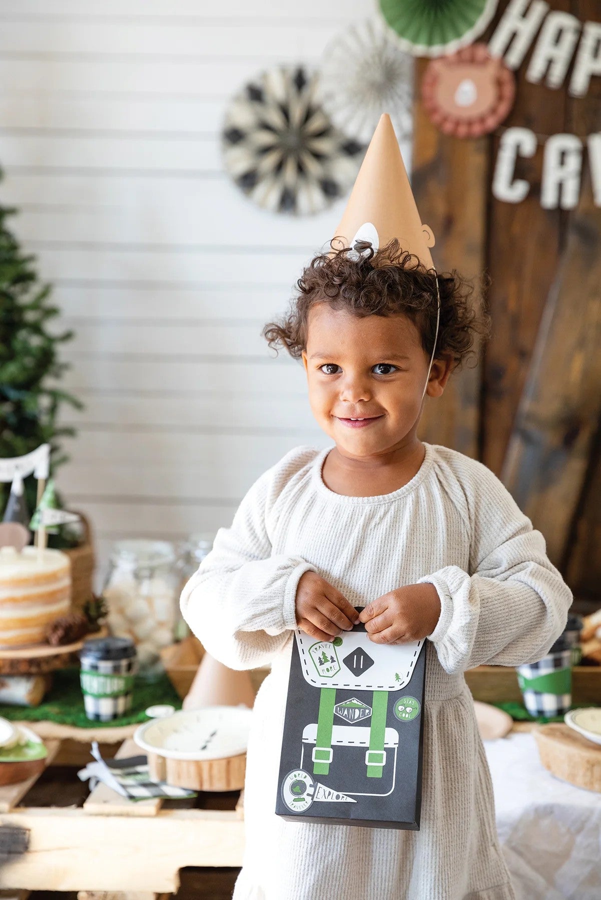 Child with adventure backpack - treat bag wearing a party hat with a 'Happy Birthday' sign in the background
